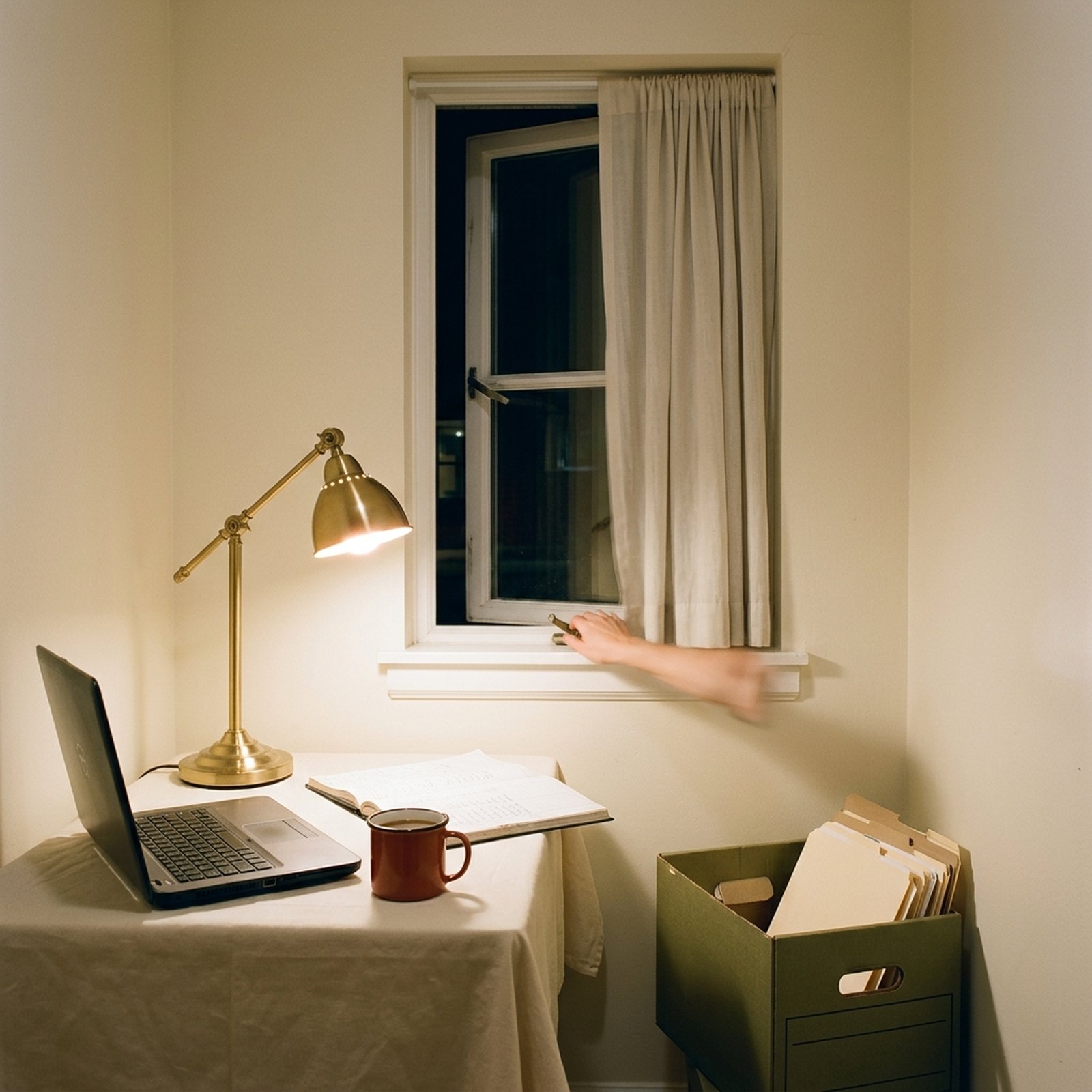 An office window left ajar in the evening above a work desk with a half-closed laptop