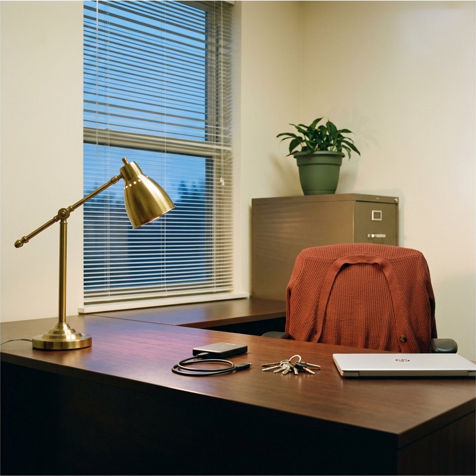 Un disque dur externe et un trousseau de clés posés sur le bureau d'un petit local, en fin de journée, sous une lampe en laiton